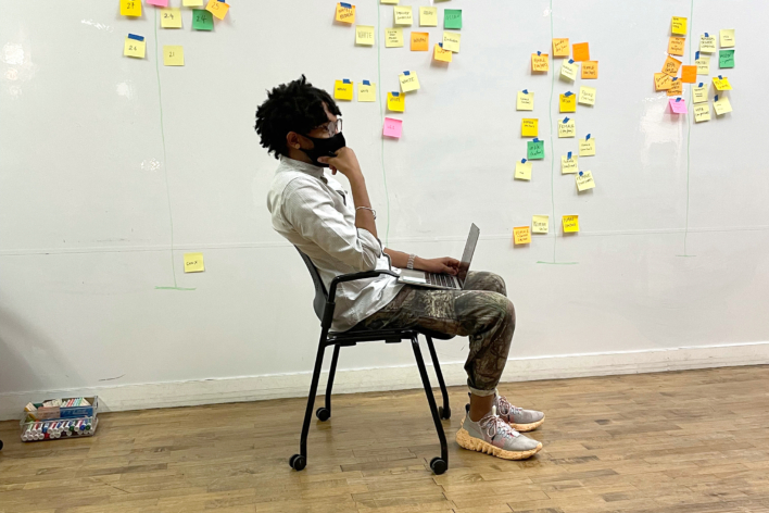 DSI Designer In Resident Shawn Harris sitting in front of a whiteboard with Post-It notes.
