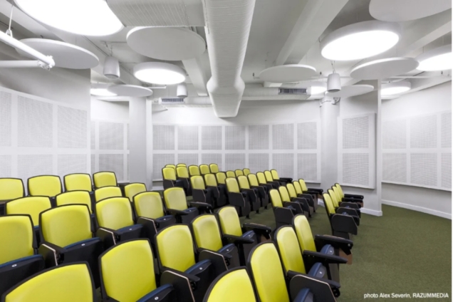 image shows a domed auditorium space with fluorescent lighting. The image shows rows of auditorium-style chairs in lime green.