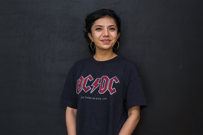 Diva Gohil wearing a navy AC/DC t-shirt and smiling at the camera.