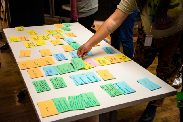 index cards with handwriting on a table as someone reaches to pull one