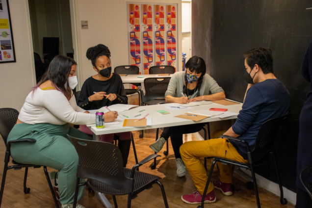 four people around a table in the process of writing and listening