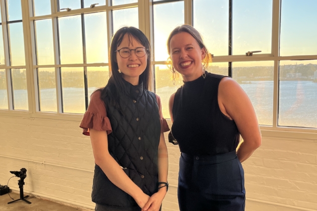 Maggie Wong and Carolyn Cesarotti smiling for the camera with a large glass window behind them.