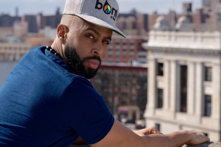 Henry Obispo looking over his right shoulder at the camera. In the background we can see buildings in the skyline of the Bronx.