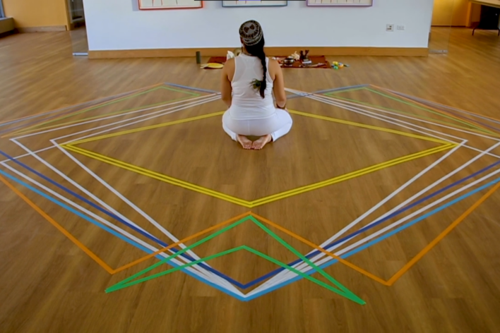 An image of a woman sitting in the middle of a complex arrangement of multicolored lines. Her back is facing the camera.