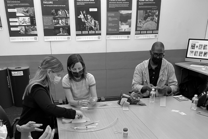 Weill Cornell Med Students and DSI faculty sitting at a table with a set of instructional posters behind them.