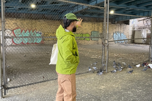 An image of a man wearing a green hat and bright green jacket pointing at something away from the camera.