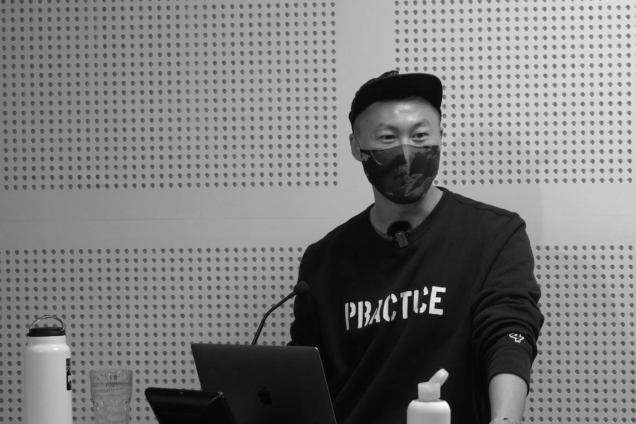 An Asian man wearing a face mask, standing at a podium giving a presentation.