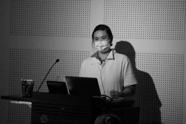 A woman wearing a mask standing at a podium and giving a presentation.