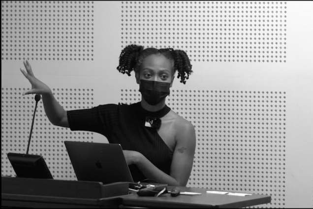 A black, female-presenting person standing at a podium.
