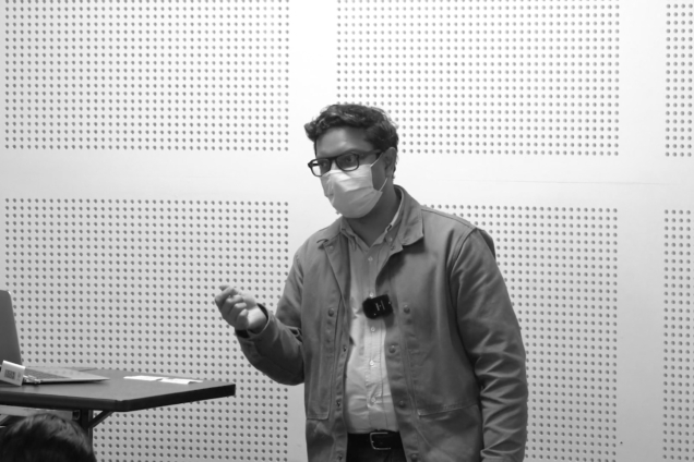 A brown-skinned man with glasses standing at a podium giving a presentation.