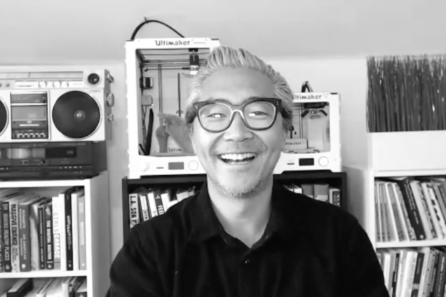 A black and white screenshot of a man wearing a black shirt looking at the camera.