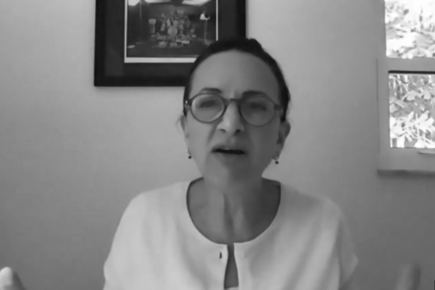 A black and white screenshot of a woman wearing a white top looking at the camera.