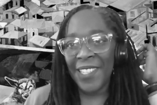 A black and white screenshot of a woman with glasses and headphones looking at the camera.