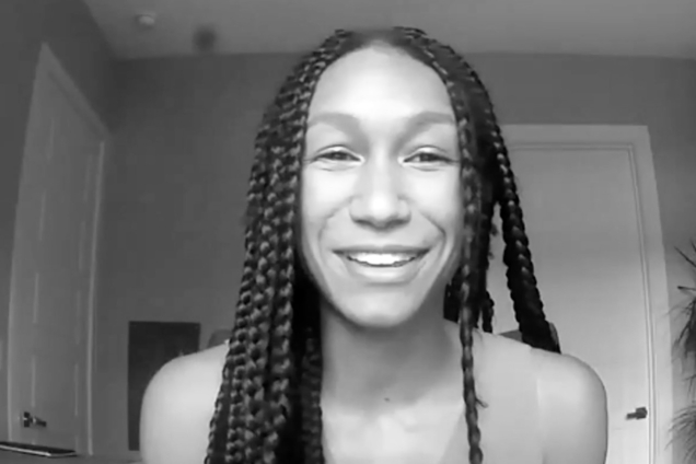 A black and white screenshot of a woman with braids looking at the camera.