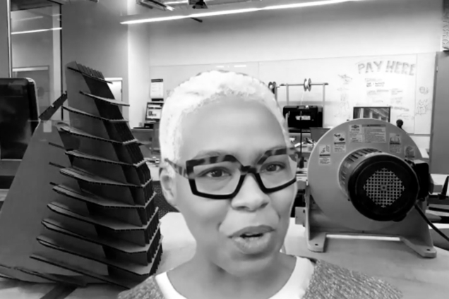 A black and white screenshot of a woman with an icy blonde pixie cut and thick black glasses looking at the camera.