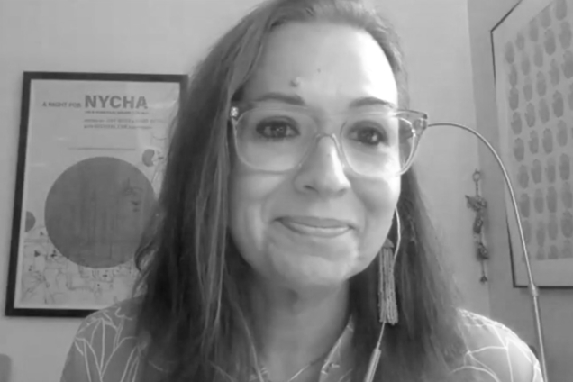 A black and white screenshot of a woman wearing a button down shirt looking at the camera.