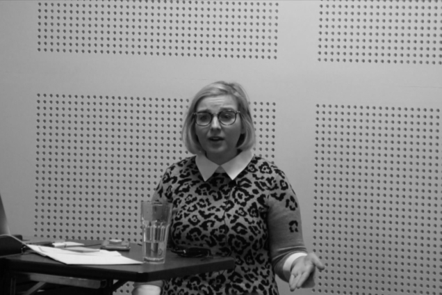 A woman with blonde hair standing at a podium giving a presentation.