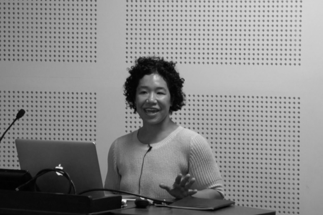 A woman with curly hair standing at a podium giving a presentation.