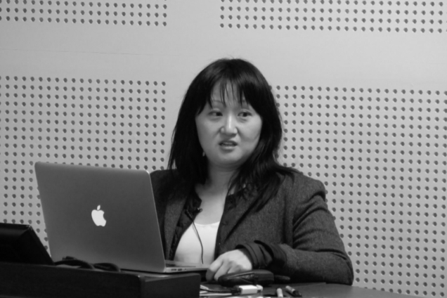 A woman standing at a computer on a podium giving a speech.