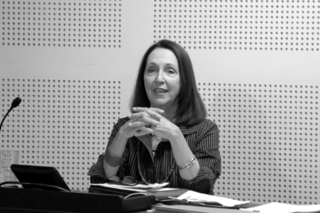 A white woman standing at a podium giving a presentation.