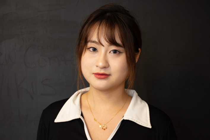An image of a woman wearing a white collared black shirt smiling at the camera.