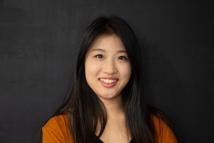 A woman wearing an orange top smiling at the camera.