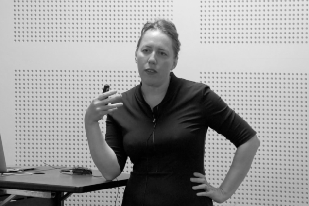 A white woman wearing a black button-down shirt giving a presentation.
