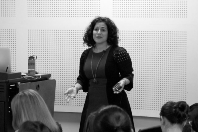 A woman with curly hair in a dark dress giving a presentation.