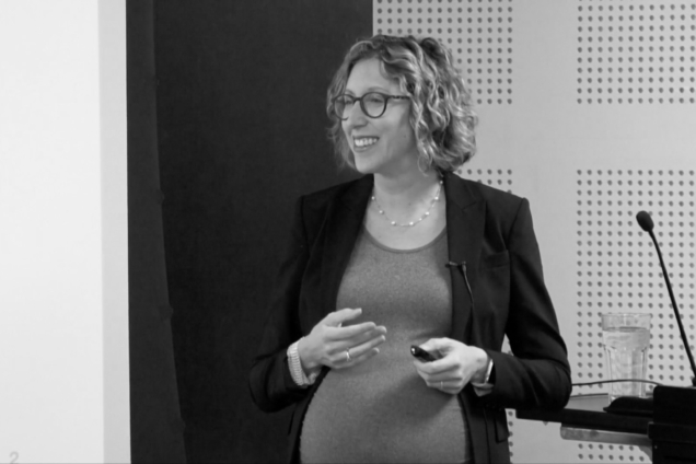A woman wearing a suit jacket, smiling at her audience.