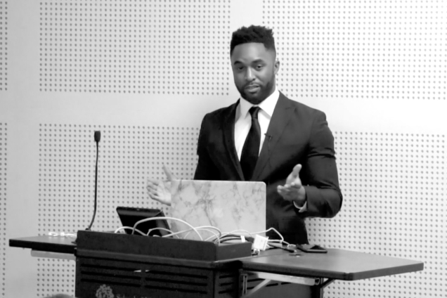 A black man in a suit giving a presentation at a podium.