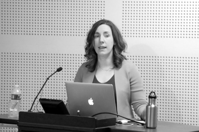 A woman in a light cardigan at a podium giving a speech.