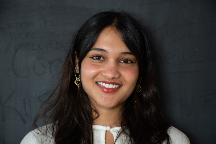 An image of a brown-skinned woman wearing white top, smiling for the camera.