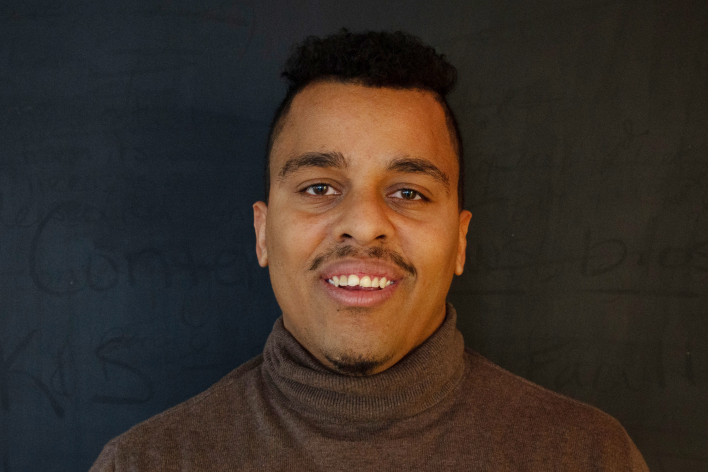A man in a brown shirt smiling at the camera.