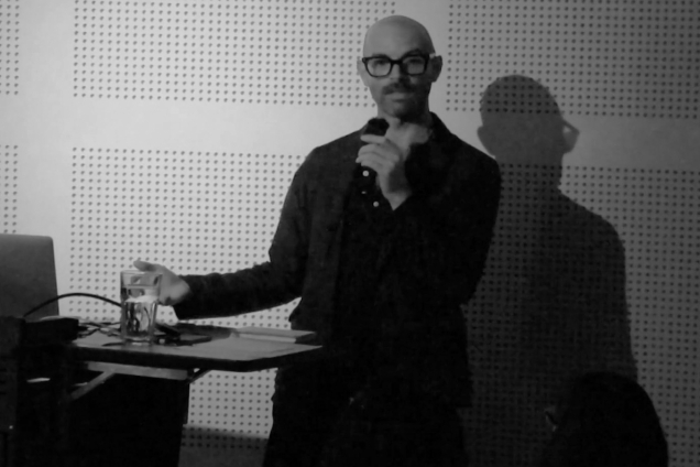 A man in a shirt, giving a presentation at a podium
