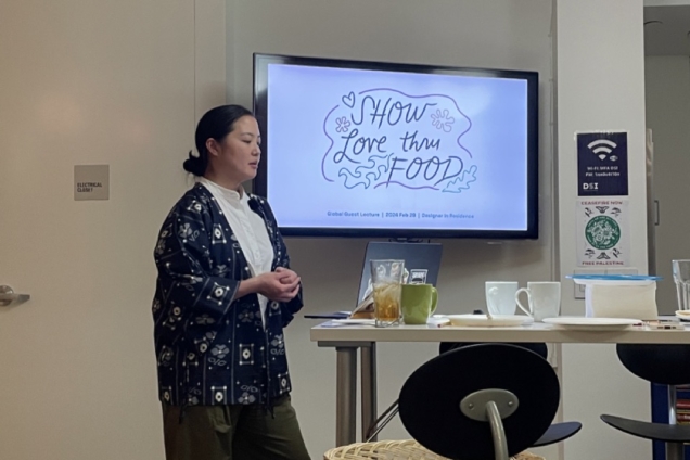 Mari Nakano speaking in front a large TV screen