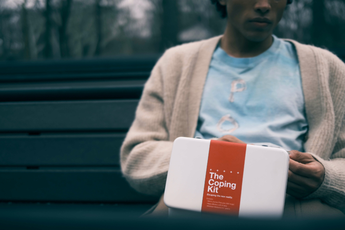 Amazonia A Worst Case Scenario Store image of a person with brown skin in a pink cardigan and white tshirt holding a white kit with a red band that says 