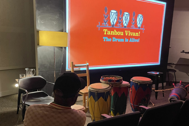 A slide presentation that says Tanbou Vivan! The Drum is Alive! on a read background in the MFA DSI auditorium