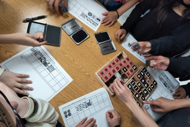 People around a table using COMPA Stamps to print on paper.