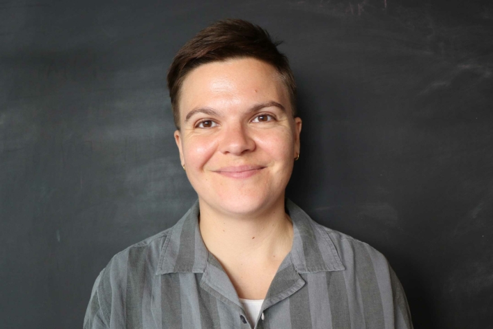 A person with brown short hair in a grey button down shirt.