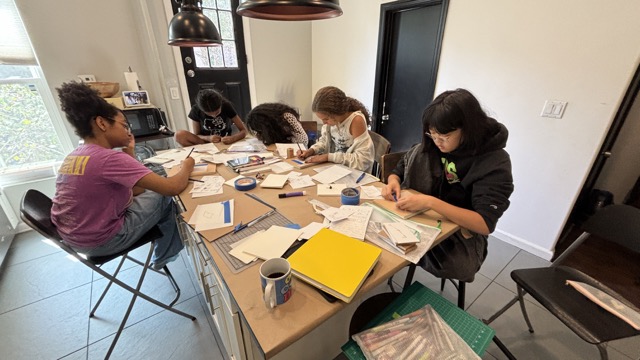 A group of Young Creative teen girls at a table working on artwork.