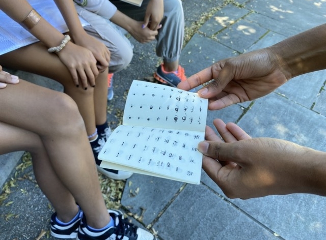 Hands holding open a small zine of symbols to a seated crowd.