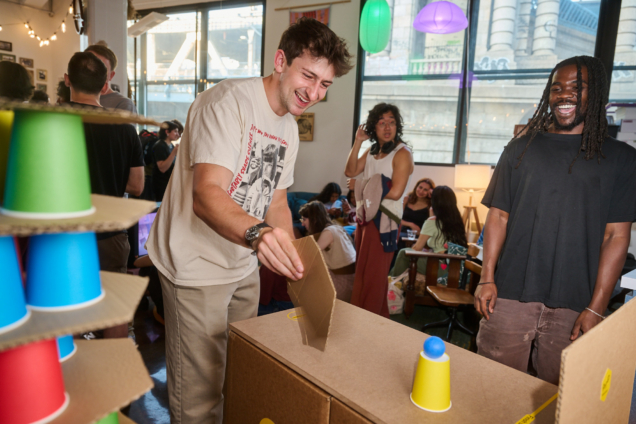 Two men at the Aging in Play game station, trying to move a ping pong ball with a fan.