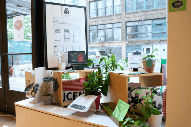 Exhibition setup against window with big poster, plants, and iPad.